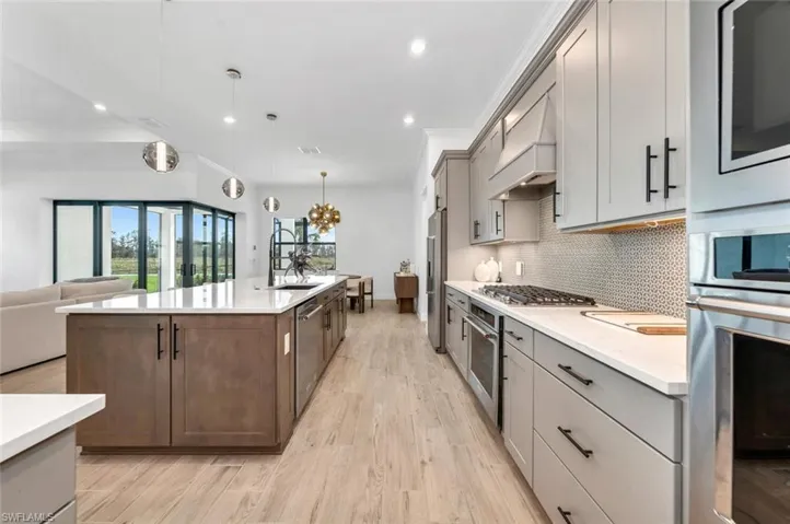 Kitchen with stainless steel appliances, decorative light fixtures, custom exhaust hood, light hardwood / wood-style flooring, and a center island with sink
