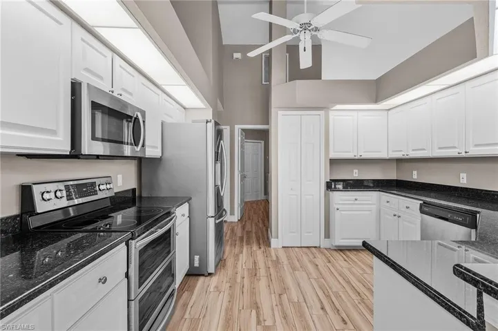 Kitchen featuring ceiling fan, dark stone countertops, light hardwood / wood-style floors, white cabinetry, and stainless steel appliances