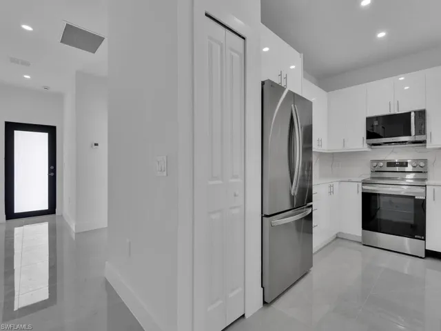 Kitchen with recessed lighting, stainless steel appliances, white cabinets, modern cabinets, and light stone countertops