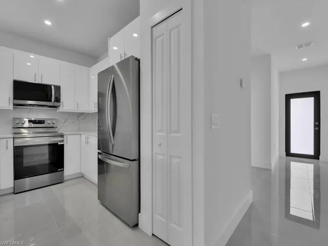 Kitchen with stainless steel appliances, recessed lighting, white cabinets, light stone counters, and modern cabinets