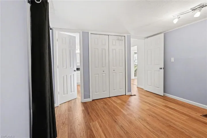 Unfurnished bedroom featuring a closet, light wood-type flooring, a textured ceiling, ornamental molding, and rail lighting
