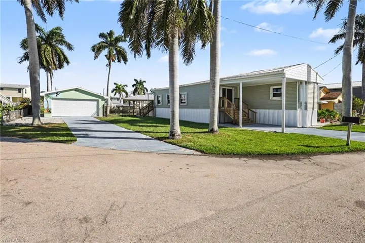 View of front of property featuring a front lawn, a detached garage, driveway, and an outbuilding