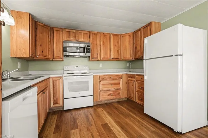 Kitchen featuring white appliances, light countertops, dark wood finished floors, and wood finish cabinetry