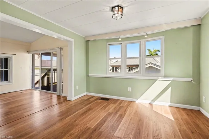 Empty room with wood finished floors, ornamental molding, vaulted ceiling, and rail lighting