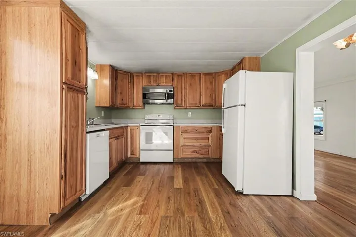 Kitchen featuring white appliances, light countertops, wood finish cabinetry, and dark wood-style floors
