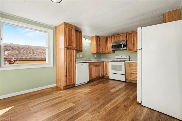 Kitchen with white appliances, wood finish cabinets, light countertops, and dark wood-type flooring