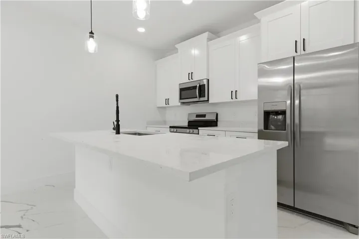 Kitchen island with a built-in sink and matte black faucet, complemented by white cabinetry, stainless steel appliances, and white stone-finish countertops