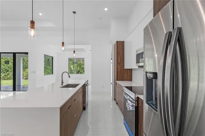 Kitchen with a raised ceiling, an island with sink, stainless steel appliances, decorative light fixtures, and sink
