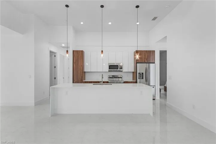Kitchen with a center island with sink, stainless steel appliances, decorative light fixtures, and light tile patterned floors