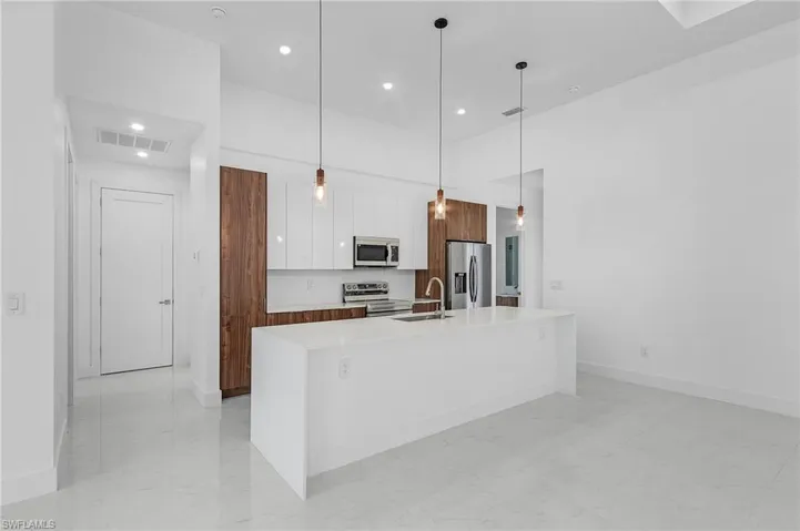 Kitchen featuring stainless steel appliances, white cabinets, pendant lighting, sink, and a kitchen island with sink