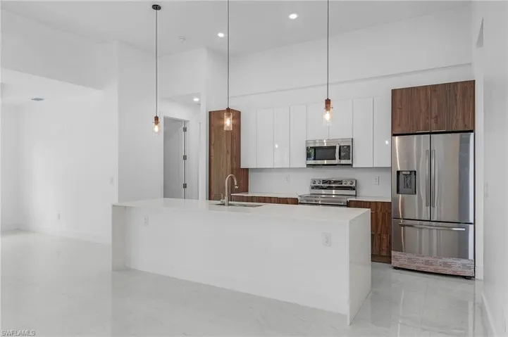 Kitchen featuring appliances with stainless steel finishes, white cabinets, a center island with sink, sink, and decorative light fixtures