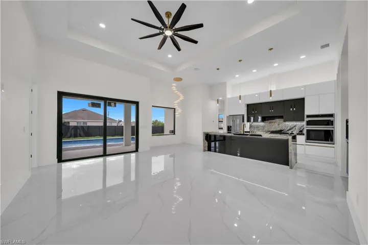 Unfurnished living room featuring ceiling fan, light marble finish flooring, a high ceiling, and recessed lighting