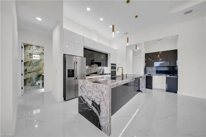 Kitchen with modern cabinets, stainless steel appliances, light marble finish flooring, an island with sink, and pendant lighting
