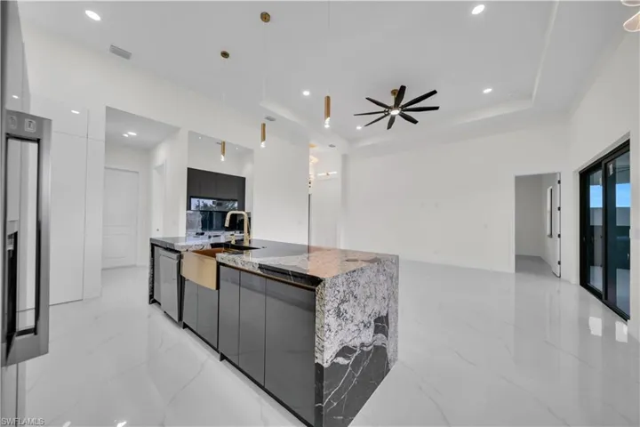 Kitchen with modern cabinets, hanging light fixtures, light marble finish floors, light stone counters, and a large island