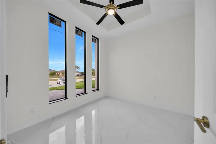 Unfurnished room with a tray ceiling, ceiling fan, and light marble finish flooring