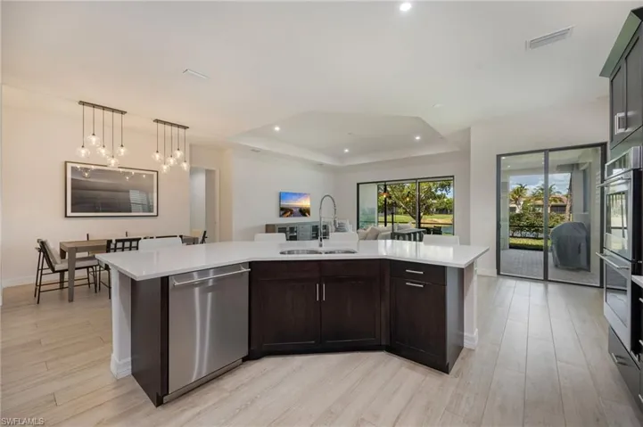 Kitchen with dark wood finish cabinetry, open floor plan, an island with sink, stainless steel appliances, and light wood-style floors