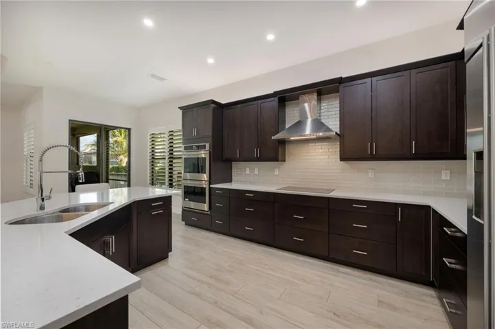 Kitchen featuring dark wood finish cabinets, light stone counters, stainless steel appliances, recessed lighting, and light wood-style floors