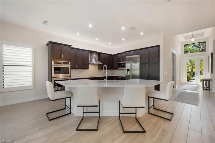 Kitchen with stainless steel appliances, dark wood finish cabinetry, a breakfast bar area, light wood-type flooring, and a large island