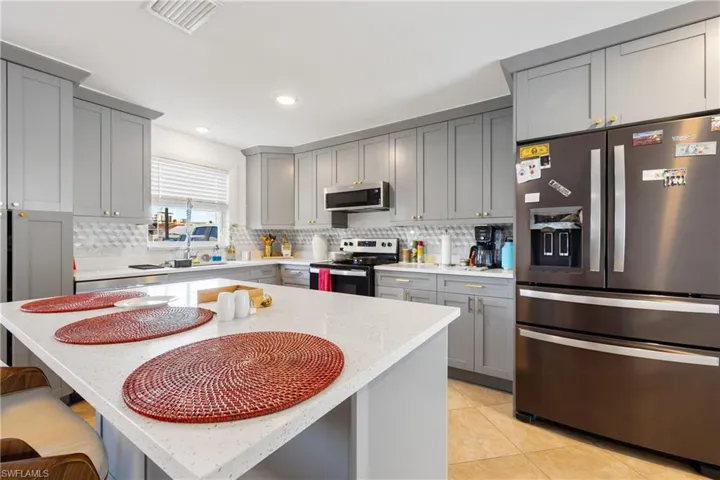 Kitchen featuring gray cabinetry, appliances with stainless steel finishes, a kitchen island, a breakfast bar, and light tile patterned floors