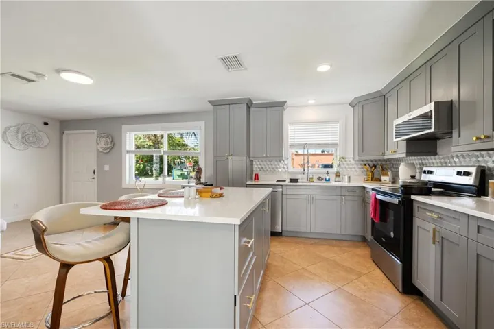 Kitchen with stainless steel electric range, a healthy amount of sunlight, tasteful backsplash, and a kitchen island