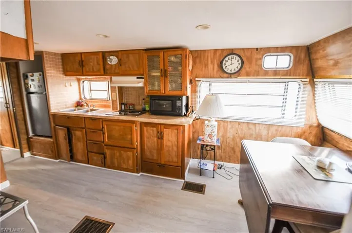 Kitchen featuring light countertops, brown cabinetry, glass insert cabinets, stainless steel appliances, and wooden walls