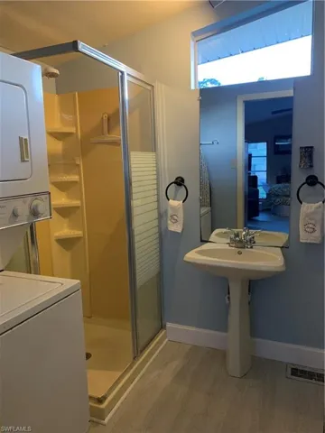 Bathroom featuring a stall shower, stacked washer and clothes dryer, and light wood-style floors