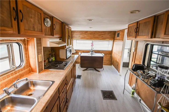 Kitchen with brown cabinetry, under cabinet range hood, black electric stovetop, stainless steel microwave, and light countertops