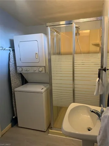 Full bath featuring a stall shower, light wood finished floors, and stacked washing machine and dryer