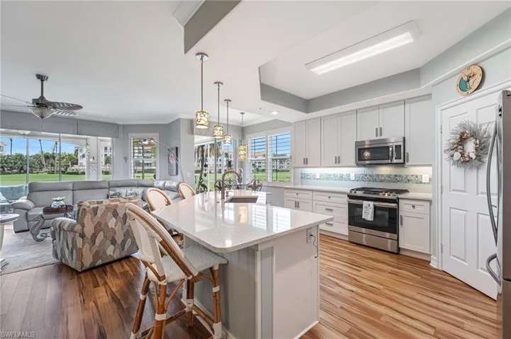 The stunning kitchen showcases sparkling quartz countertops, a colorful backsplash, and 42-inch white shaker-style cabinetry with under-cabinet lighting, complemented by stainless steel appliances, a tray ceiling, and sweeping golf course views—an ideal space for entertaining while watching the chef prepare favorite meals.