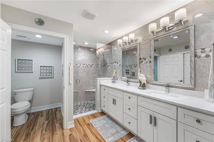 The primary bath features dual quartz-topped vanities, a dramatic tiled accent wall that extends seamlessly into the walk-in shower with a sleek glass enclosure, and a private water closet.