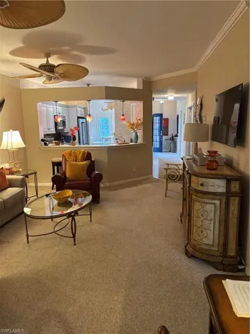 Living room featuring light colored carpet, ornamental molding, and a ceiling fan