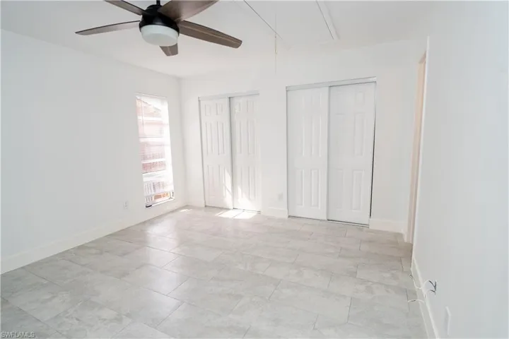Spacious room featuring light gray tile flooring, a contemporary ceiling fan, and two sets of bi-fold closet doors