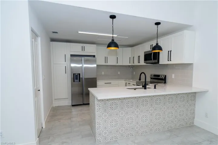 Contemporary kitchen featuring white shaker cabinetry, stainless steel appliances, a subway tile backsplash, and a patterned island facade with a white countertop