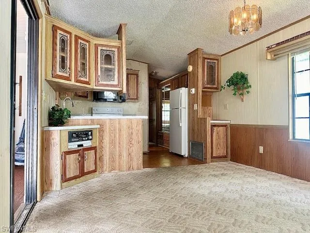 Kitchen featuring a textured ceiling, plenty of natural light, white fridge, and light carpet