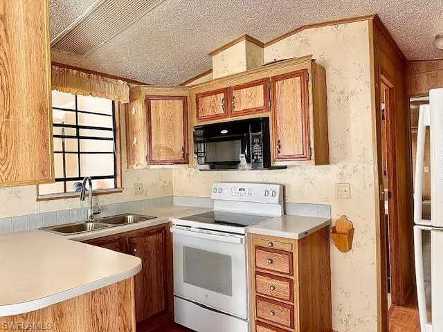 Kitchen with sink, a textured ceiling, white appliances, and parquet flooring