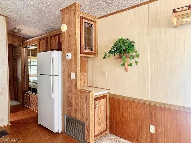 Kitchen with parquet floors, white refrigerator, and a textured ceiling