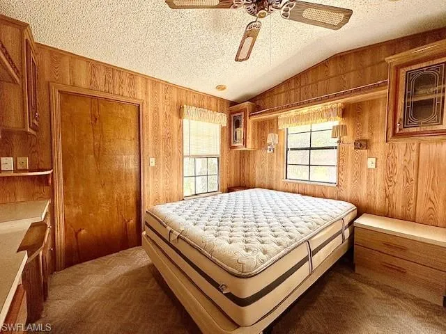 Carpeted bedroom featuring multiple windows, wooden walls, and a textured ceiling