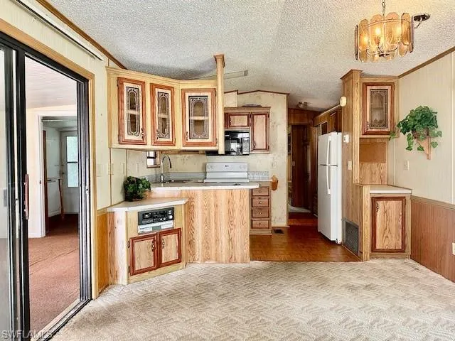 Kitchen featuring sink, white appliances, a textured ceiling, and light colored carpet