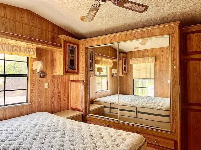 Bedroom with ceiling fan, wood walls, a closet, vaulted ceiling, and a textured ceiling