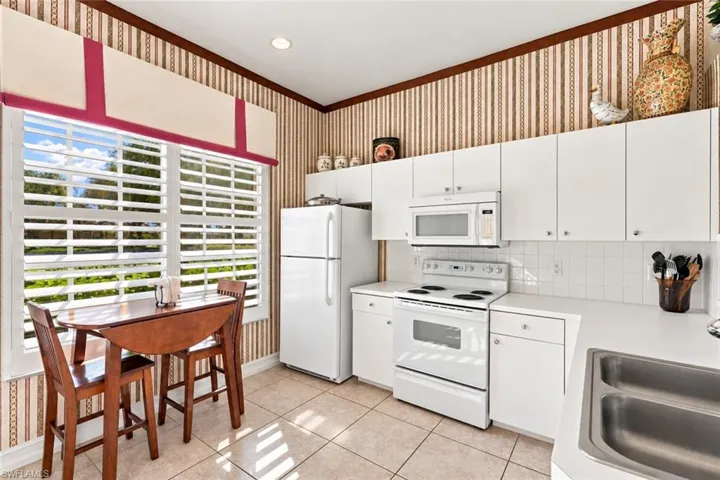 Kitchen featuring white cabinetry, solid-surface countertops, tile flooring, and integrated white appliances, accented by plantation shutters