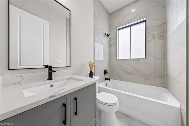 Full bath with vanity, a combined bath / shower with marble appearance, and light marble finish floors