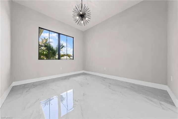 Empty room featuring lofted ceiling, light marble finish flooring, and suspended lighting