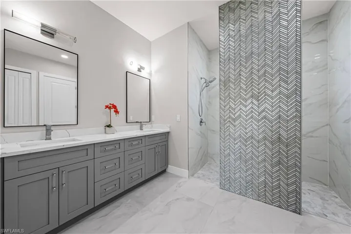 Bathroom with double vanity, a marble finish shower, and light marble finish floors