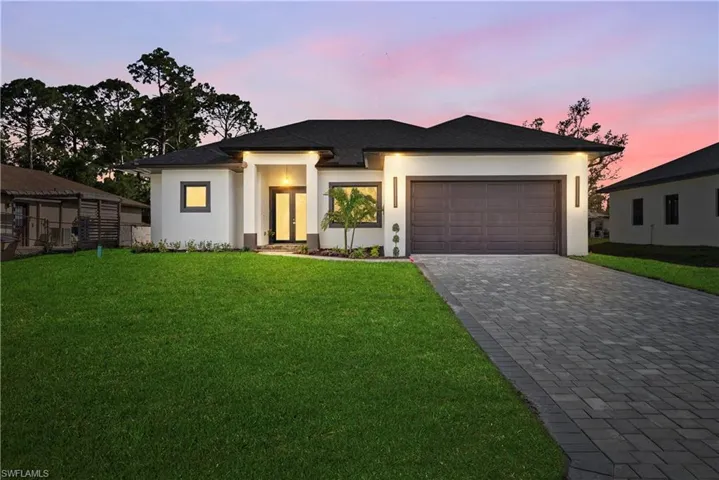 Prairie-style home with a lawn, decorative driveway, an attached garage, and stucco siding