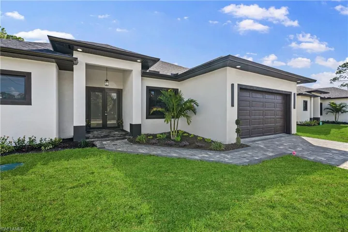 View of front facade with french doors, a front yard, stucco siding, and a garage