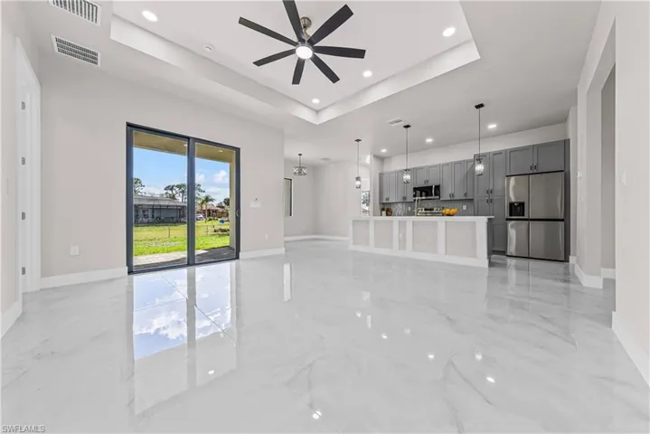 Unfurnished living room featuring a tray ceiling, a ceiling fan, light marble finish flooring, and recessed lighting