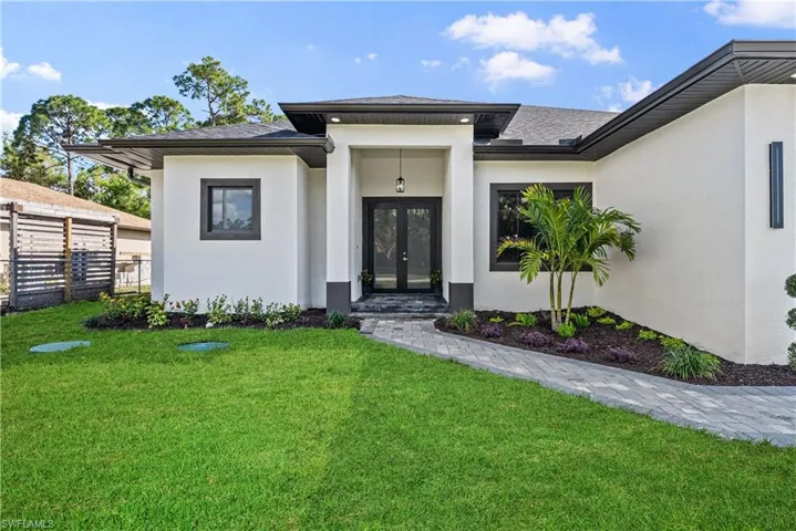Entrance to property with french doors, a lawn, stucco siding, and roof with shingles