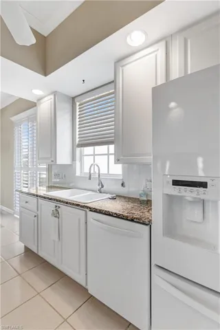 Kitchen with white appliances, a sink, white cabinets, light tile patterned flooring, and decorative backsplash