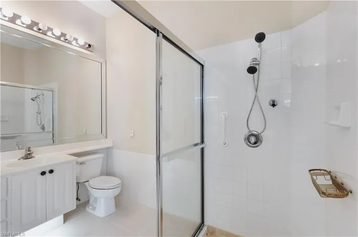 MB with a tile shower, toilet, vanity, and tile patterned flooring