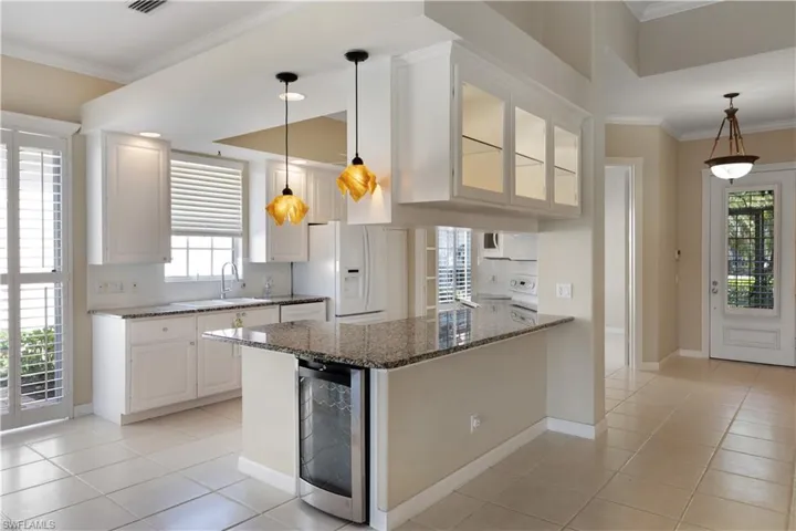 Kitchen with beverage cooler, white appliances, a sink, dark stone counters, and light tile patterned flooring